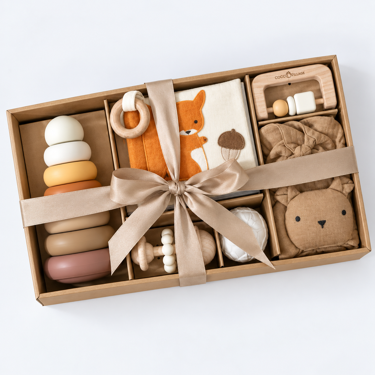 A wooden toy gift set in a brown cardboard box, tied with a beige ribbon. The set includes a wooden stacking ring toy, a plush fox rattle, a fabric acorn toy, a wooden bead tray, a soft brown cloth item, and a bear-shaped cloth item, all arranged on a white background.