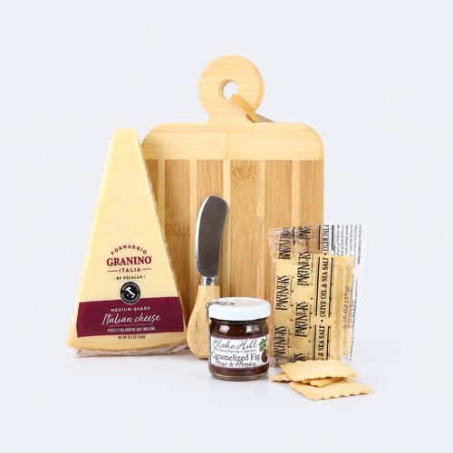 A gourmet cheese and crackers gift set arranged on a light gray background, featuring a wedge of Parmigiano d'Orino Italian cheese, a bamboo cutting board, a small cheese knife, a jar of prosciutto crudo, packaged prosciutto, and flatbread crackers.