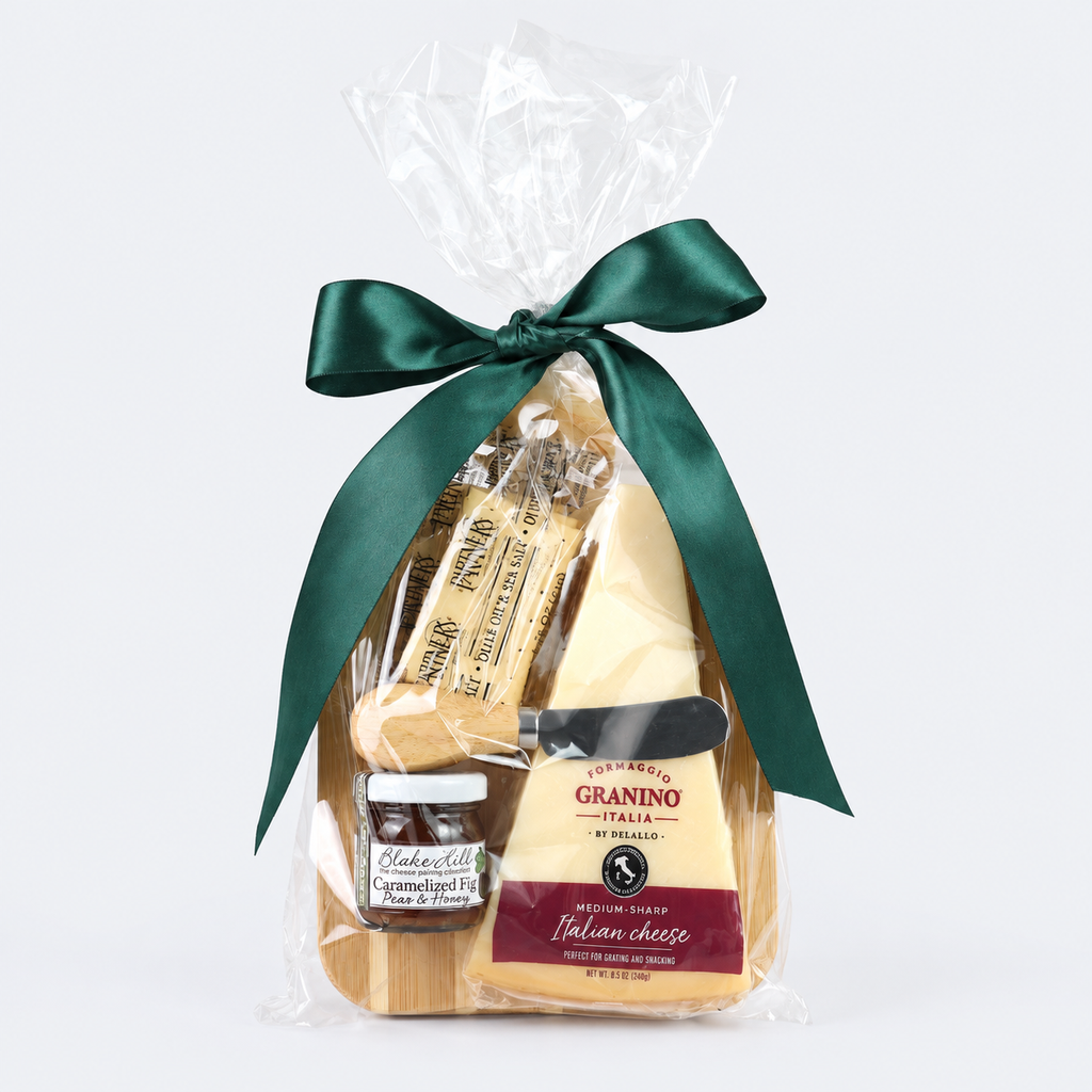 A gourmet cheese and charcuterie gift basket packaged in clear cellophane with a dark green satin bow. The basket contains a wedge of Parmesan Granino cheese, two sticks of salami, and a small jar of cured meats, all arranged on a light wood base against a white background.