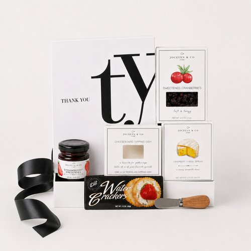 A curated gift box set from Jessica & Co. arranged on a white marble surface, featuring a white 'Thank You' card, a jar of preserves, water crackers, cranberry sauce, cheese spread, a small knife, and a black textured insert inside a gift box.